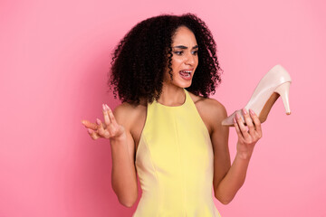 Young woman in stylish yellow dress holding a white high heel shoe against pink background,...