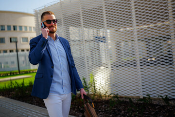Young businessman walking outside an office building, chatting on the phone after work. Carrying a briefcase and wearing sunglasses, exuding confidence and style