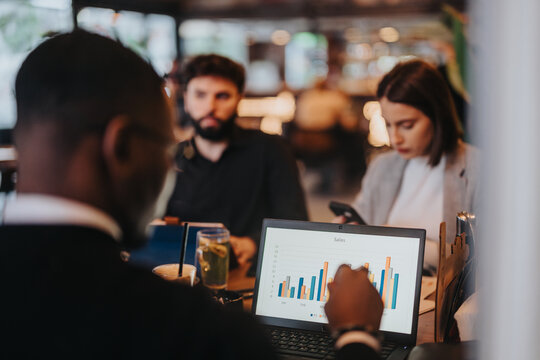 A group of professionals collaborates and discusses sales performance, analyzing graphs on a laptop.