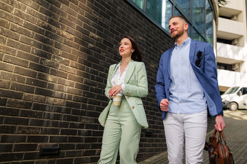 Two young businesspeople walking along a bustling city street, sipping coffee and engaging in a lively conversation after a productive day at work, embodying teamwork and success