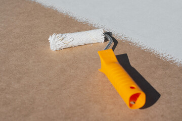 Close-up a paint roller with a yellow handle applying a smooth layer of white paint onto a brown surface. Concept home renovation and DIY projects.