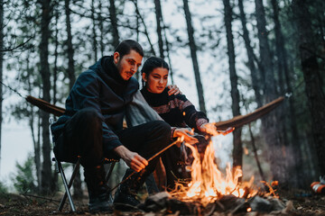 A couple sits by a bonfire in a winter forest setting, enjoying time together. The serene...