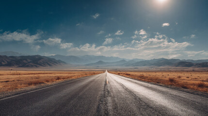 A long, open road leads towards distant mountains under a bright blue sky.