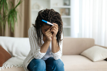 Black woman holding a pregnancy test and crying, emotional and overwhelmed. Depicts anxiety, fear,...