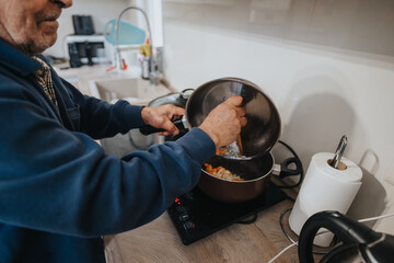A senior man cooking vegetables on an electric stove top, showcasing his culinary skills in a...