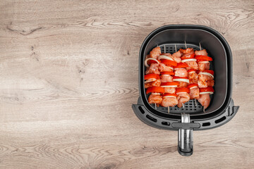 Raw chicken and vegetable skewers are neatly arranged inside an air fryer basket, ready for healthy...
