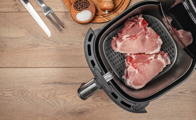 Raw pork chops are placed inside an air fryer basket, surrounded by kitchen tools and seasonings on...