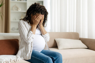 Black pregnant woman covering face with hands, showing sadness or distress. Emotional moment...
