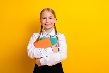 Young cheerful schoolgirl in uniform holding book against a bright yellow background showcasing...
