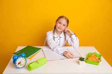 Charming schoolgirl in formal attire learning with stationery and snacks on yellow background