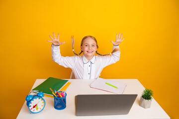 Preteen Girl Sitting at Desk with Laptop and Notebooks Against Yellow Background