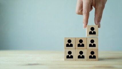Hand places wood block with person icon atop a team