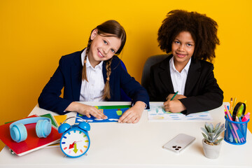 Two young schoolgirls in uniforms study at a desk surrounded by colorful supplies with a bright...