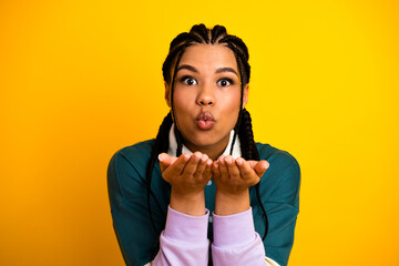 Playful young woman blowing a kiss, showcasing style and elegance with braided hair against vibrant...