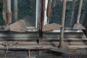 A collection of old, weathered gardening tools resting against a window, showing signs of time.