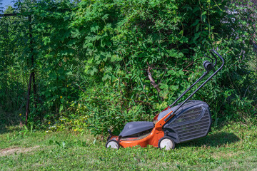 An orange lawnmower is parked on the green grass ready to mow the yard on a sunny day.