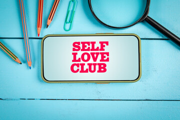 Self Love Club Message Displayed on Smartphone with Stationery on Blue Wooden Background