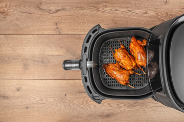 Three perfectly roasted quails with golden, crispy skin are arranged inside an air fryer basket,...