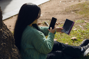 young woman in the park sitting with her cell phone and a book