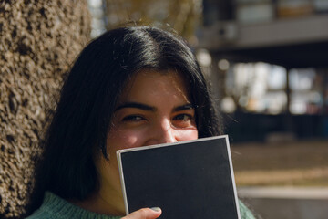 Portrait of young woman in park sitting on her face with book