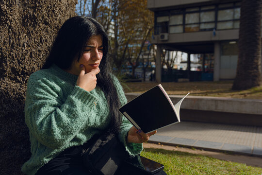 young confused woman reading a book in the park
