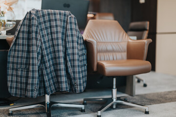 A stylish plaid blazer draped over a polished leather office chair in a contemporary office setting, suggesting business professionalism, workspace atmosphere, and workplace environment.