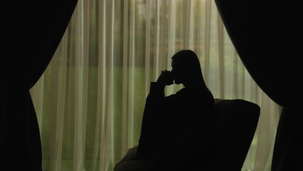 Silhouette of a distressed woman in front of backlit curtains
