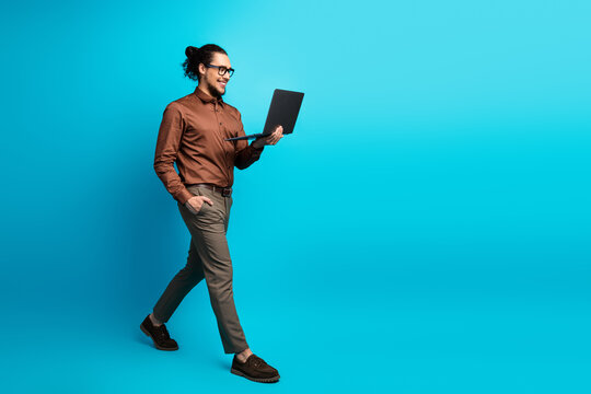 Young professional man walking with a laptop in hand against a turquoise background, dressed in elegant formalwear