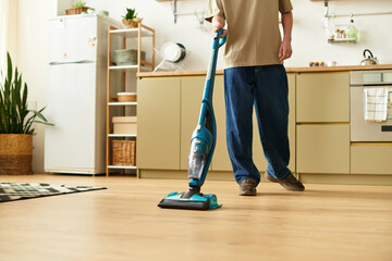 Handsome young man cleaning his modern home with a vacuum cleaner during bright daylight hours