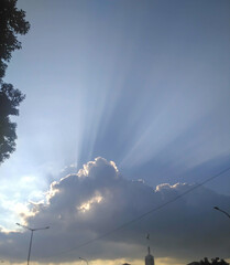 Sunlight streams through a large, puffy cloud in a bright blue sky, creating a dramatic and...