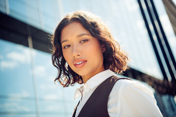 Confident professional young woman in formal attire outdoors in front of a modern urban glass...