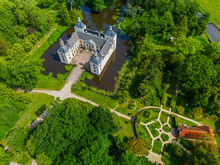 Aerial view of a historic castle surrounded by a forest, with vast green fields, winding waterways,...