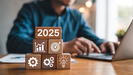 Wooden blocks display planning for year 2025 with business icons and a man using a laptop.