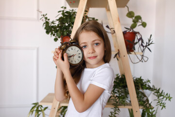 A girl holds an alarm clock in her hands