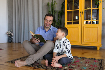 Dad sits on the floor in the room with his son and reads him a book