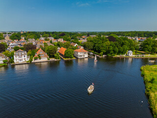 A yacht with a white sail sails along the canal. A beautiful windmill. Aerial view of narrow canal...