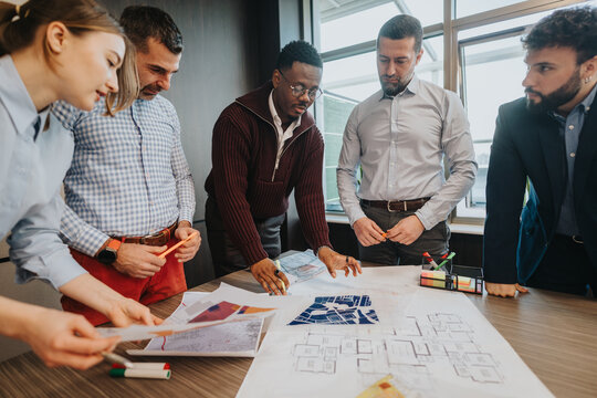 Group of professionals collaborating on design ideas, sharing opinions, and reviewing blueprints in a sunny office environment, emphasizing teamwork, innovation, and creative problem-solving.