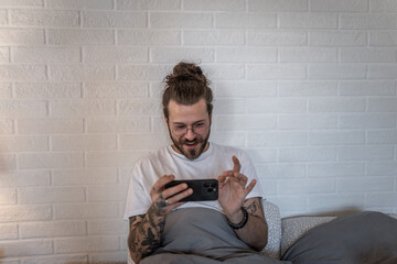 Young man playing mobile game in bed after waking up