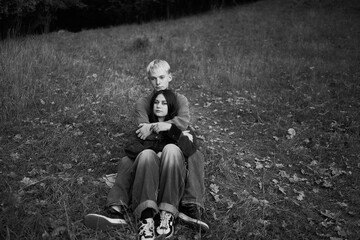 15-year-old teenage couple in love lies, sits on the grass in the park surrounded by fallen autumn...