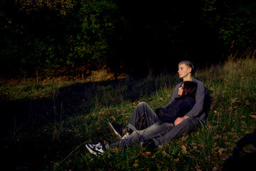 Fototapeta premium 15-year-old teenage couple in love lies, sits on the grass in the park surrounded by fallen autumn leaves
