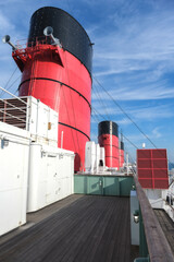 Red and black funnel of historic oceanliner ocean liner Mary against deep blue sky with clouds	