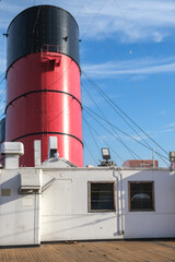 Red and black funnel of historic oceanliner ocean liner Mary against deep blue sky with clouds	