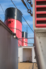 Red and black funnel of historic oceanliner ocean liner Mary against deep blue sky with clouds	