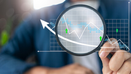 Hand holding magnifying glass analyzing financial graph, business data analysis, market trends,...