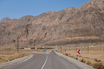 A huge mountain range rising sharply in front of the highway. A village is visible in the distance....