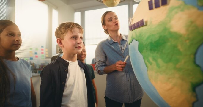 STEM Science Lesson: Female Teacher Educating Smart Diverse Kids Using Globe with Miniature 3D Models of Wind Turbines and Solar Panels. Primary School Children Studying Renewable Energy and Ecology.