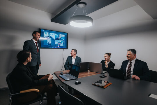 Business people in a conference room conducting a meeting with both in-person and virtual participants displayed on a monitor, showcasing teamwork and modern workplace collaboration with technology.