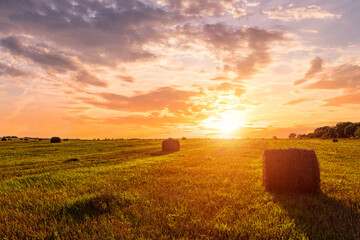 Scenic sunset over hay bales in a field. Golden light bathes the landscape, creating a tranquil...