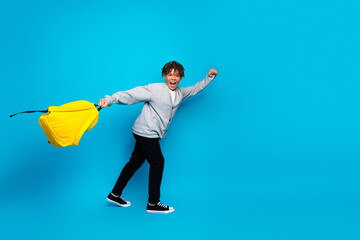 Happy young boy poses with a yellow backpack and gestures excitedly against a bright blue background