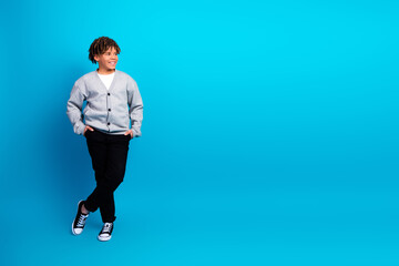 Smiling young boy in grey cardigan against blue studio background showcasing casual style and youthfulness
